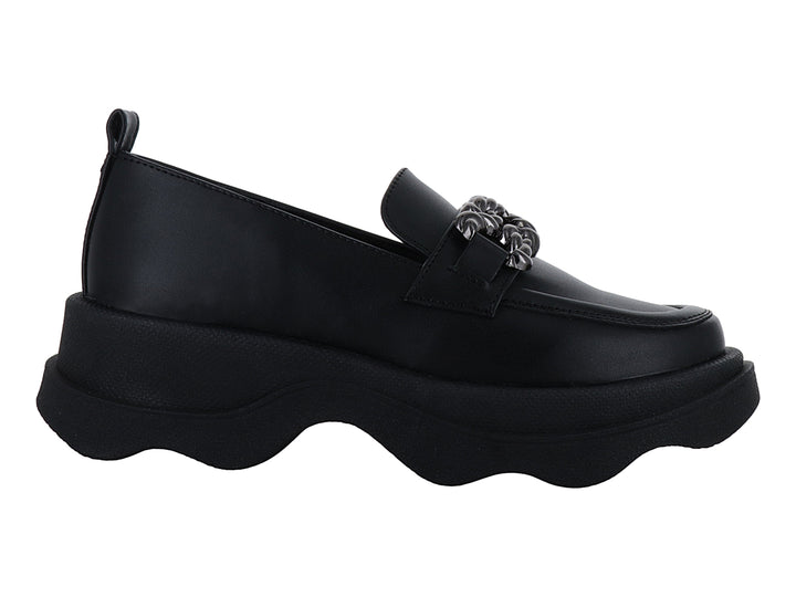 Zapato loafer negro con suela ancha ondulada y detalle metálico decorativo en la parte superior.