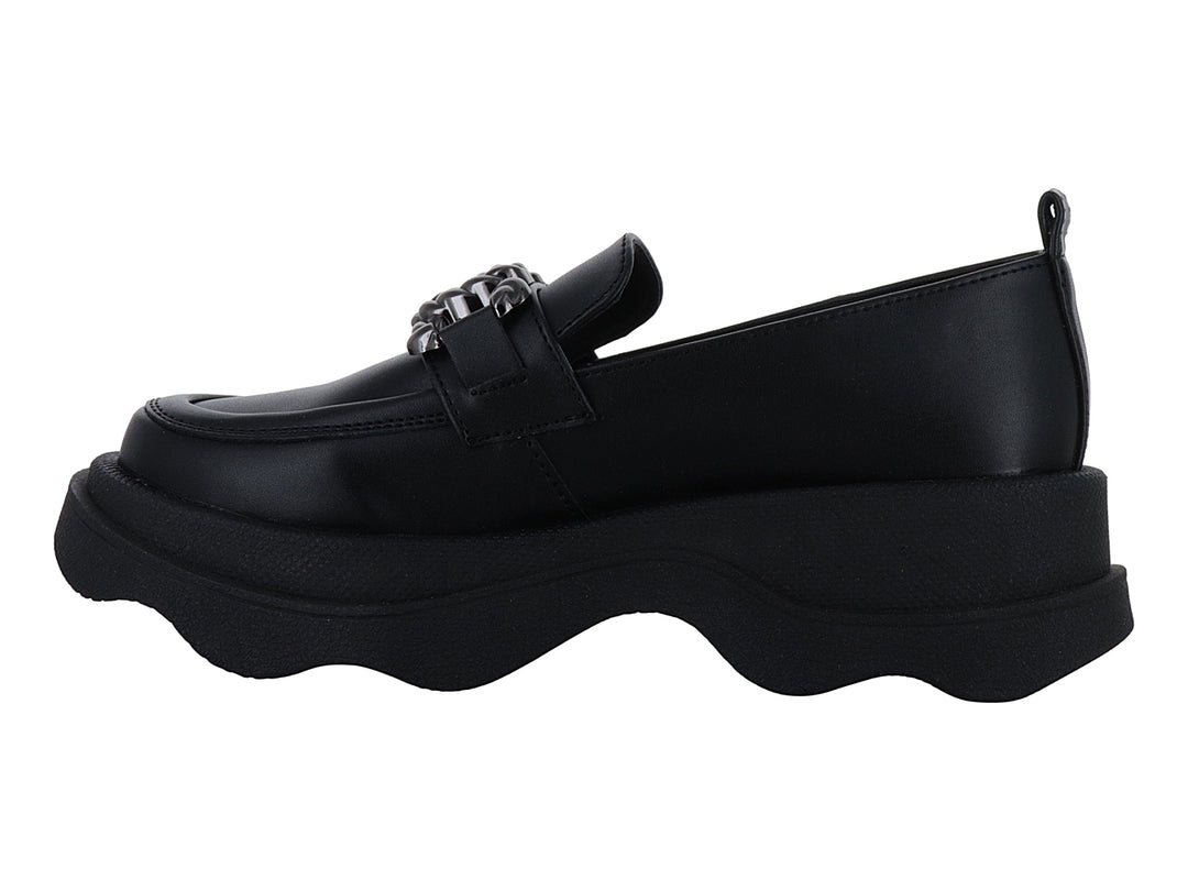 Zapato loafer negro con suela ancha ondulada y detalle metálico decorativo en la parte superior.