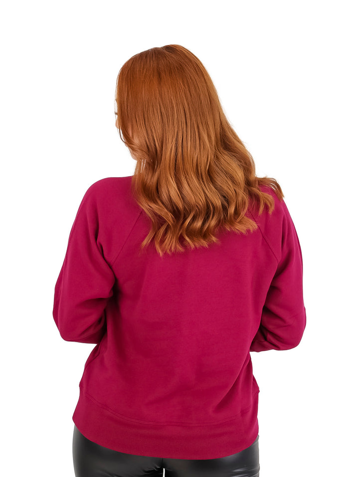 Mujer vistiendo un pullover DKNY color beetroot con cuello redondo y una línea plateada brillante en el pecho.