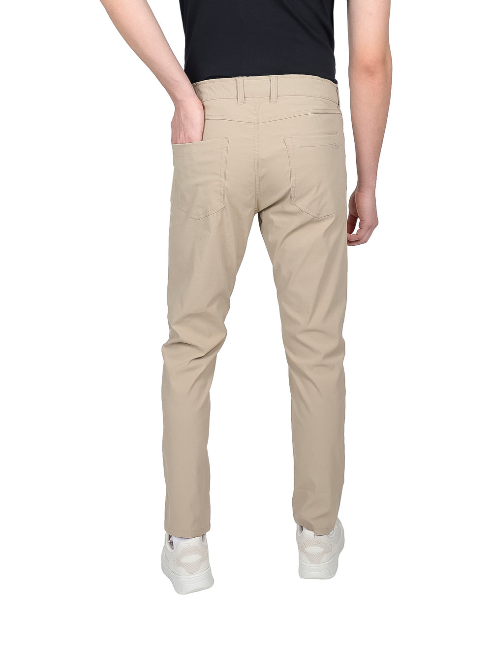Hombre vistiendo pantalones de gabardina color khaki de corte ajustado y tenis blancos.