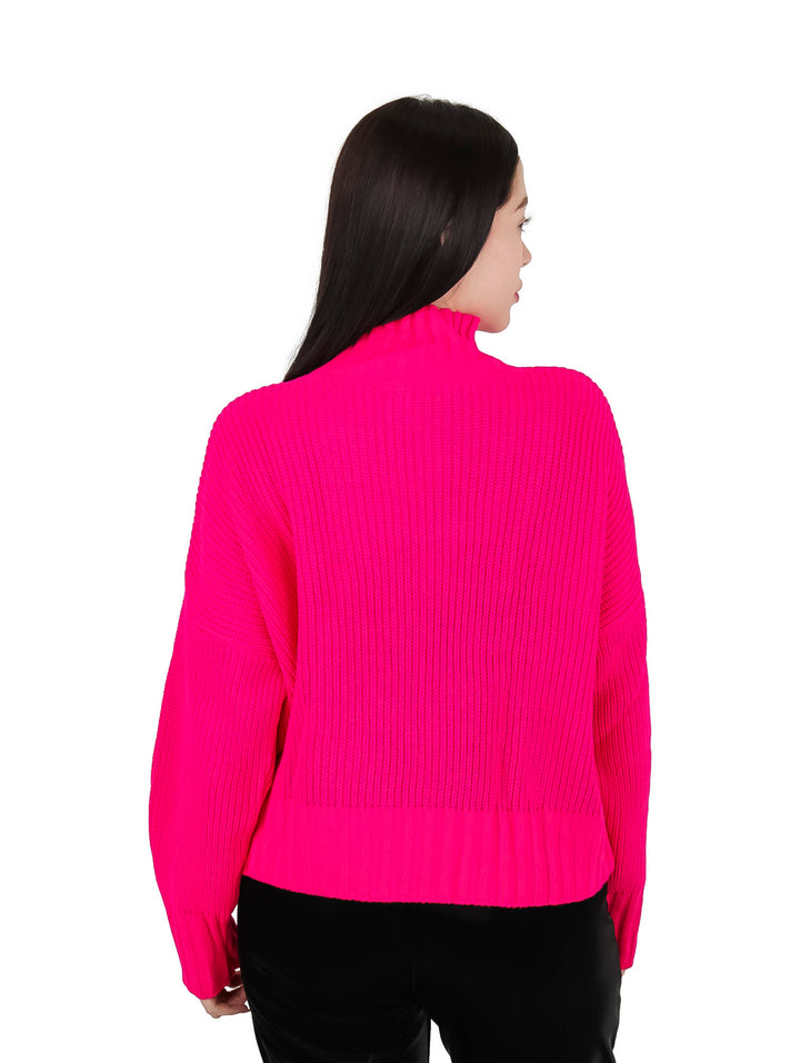 Mujer vistiendo un suéter fucsia de cuello alto adornado con piedras coloridas.