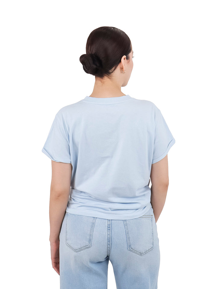 Mujer vistiendo camiseta DKNY color azul claro con nudo en la cintura y pantalones vaqueros claros.