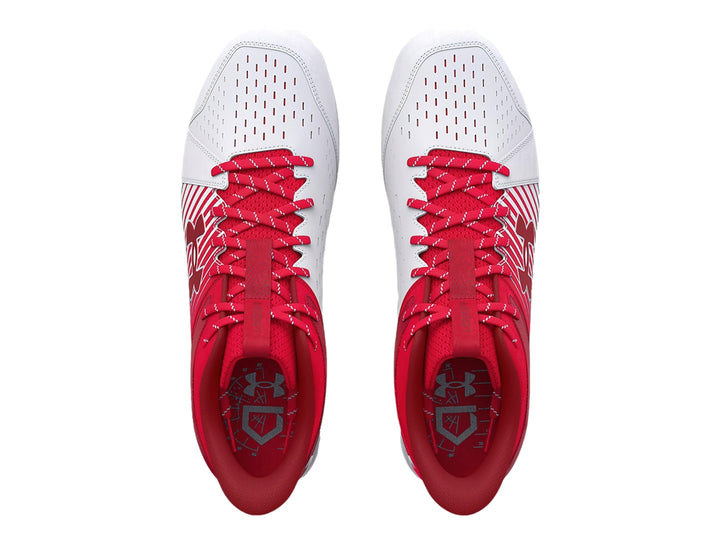 Zapato deportivo Under Armour color rojo y blanco con suela de tacos para deporte.