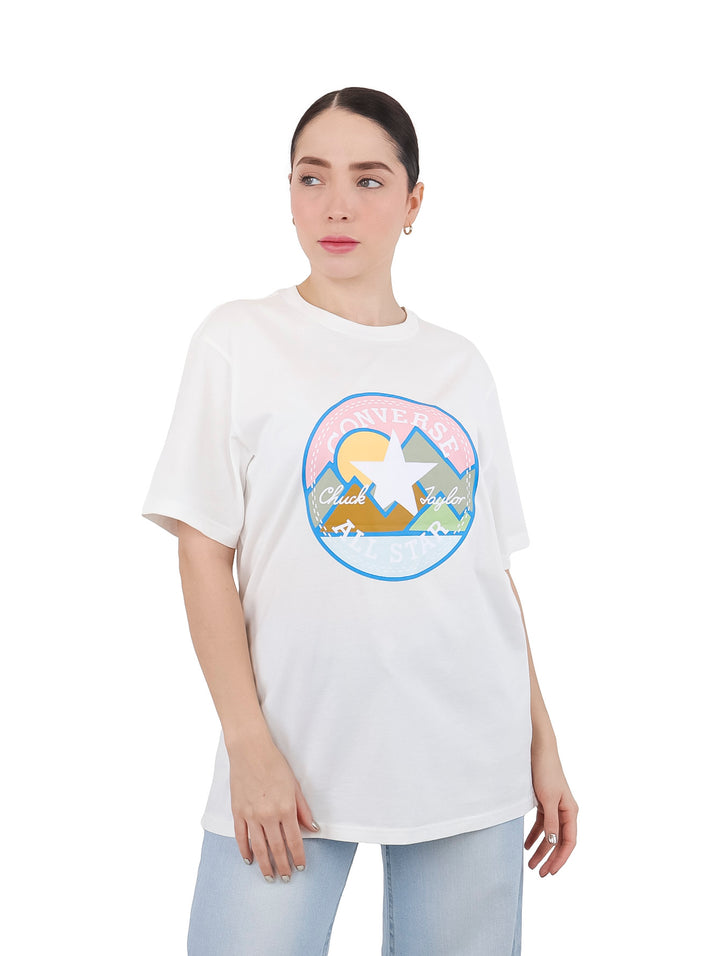 Mujer vistiendo una camiseta blanca de manga corta con un estampado circular colorido en el pecho.