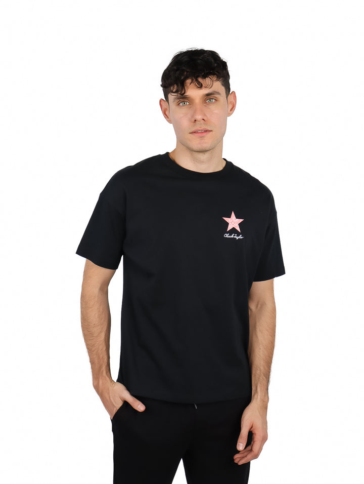 Hombre vistiendo una playera negra de manga corta Converse con una estrella rosa pequeña en el pecho.
