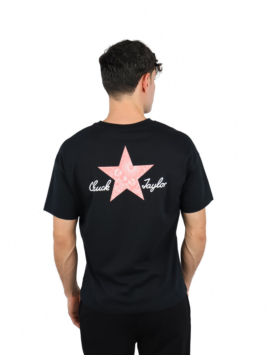 Hombre vistiendo una playera negra de manga corta Converse con una estrella rosa pequeña en el pecho.