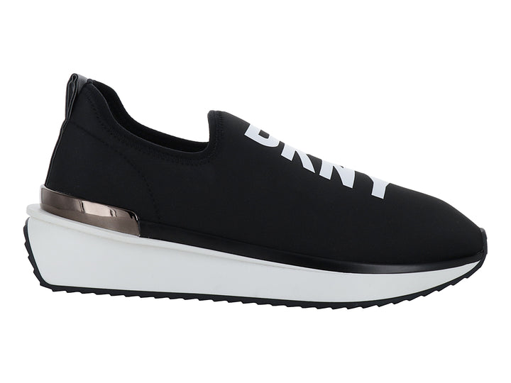 Tenis DKNY slip-on color negro con suela blanca y detalle metálico en el talón.