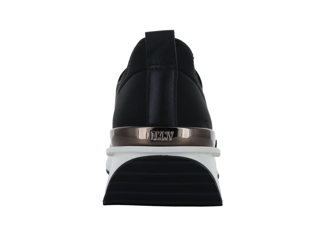 Tenis DKNY slip-on color negro con suela blanca y detalle metálico en el talón.