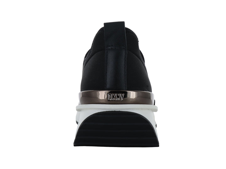 Tenis DKNY slip-on color negro con suela blanca y detalle metálico en el talón.