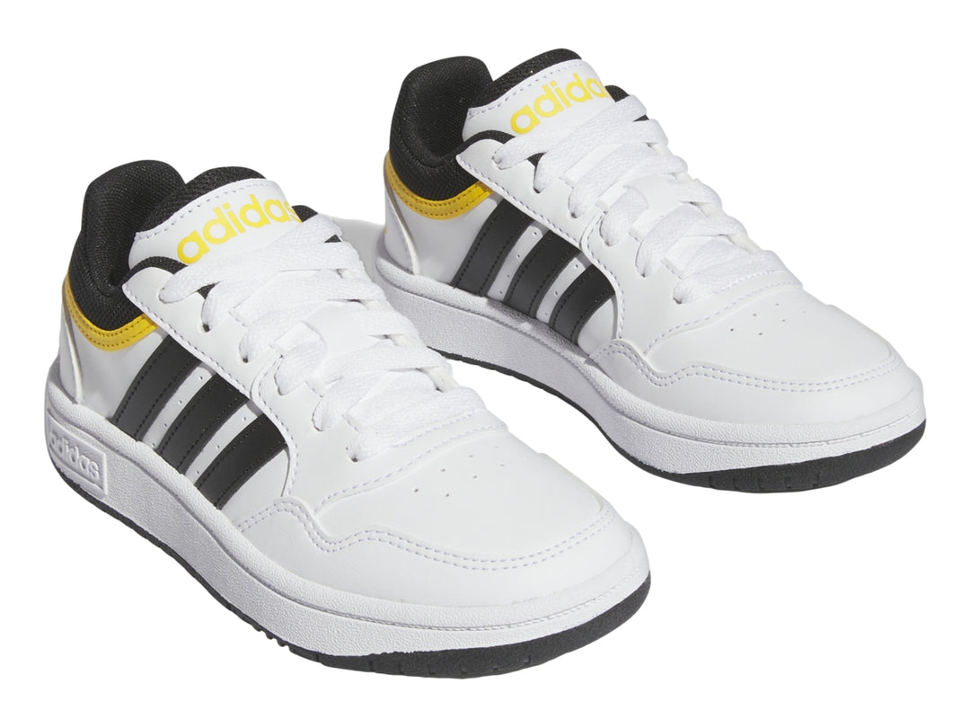 Tenis Adidas blancos con tres franjas negras y detalles en amarillo.