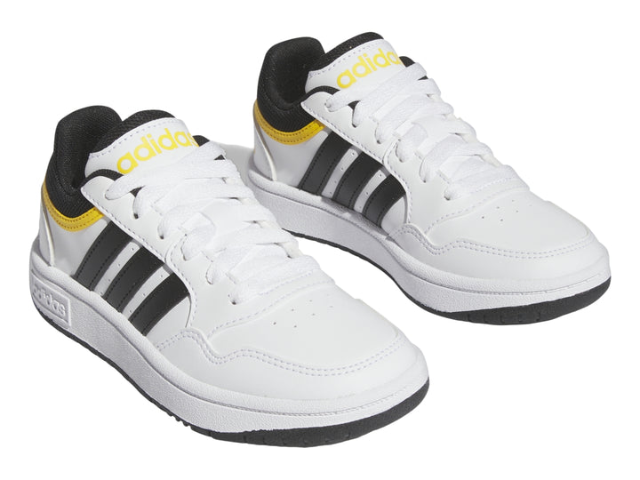 Tenis Adidas blancos con tres franjas negras y detalles en amarillo.