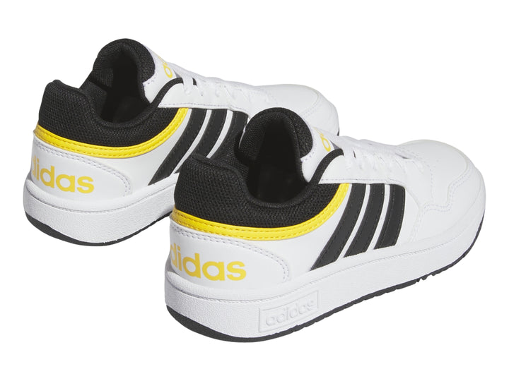 Tenis Adidas blancos con tres franjas negras y detalles en amarillo.