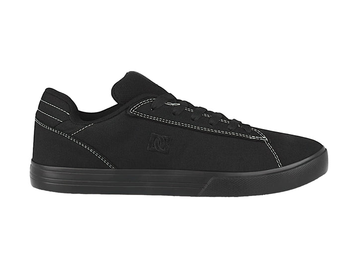 Tenis negros de tela marca DC Shoes con costuras blancas y suela plana.