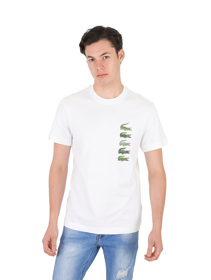 Hombre vistiendo camiseta blanca de manga corta con cuello redondo y pequeños logos verdes en el pecho.