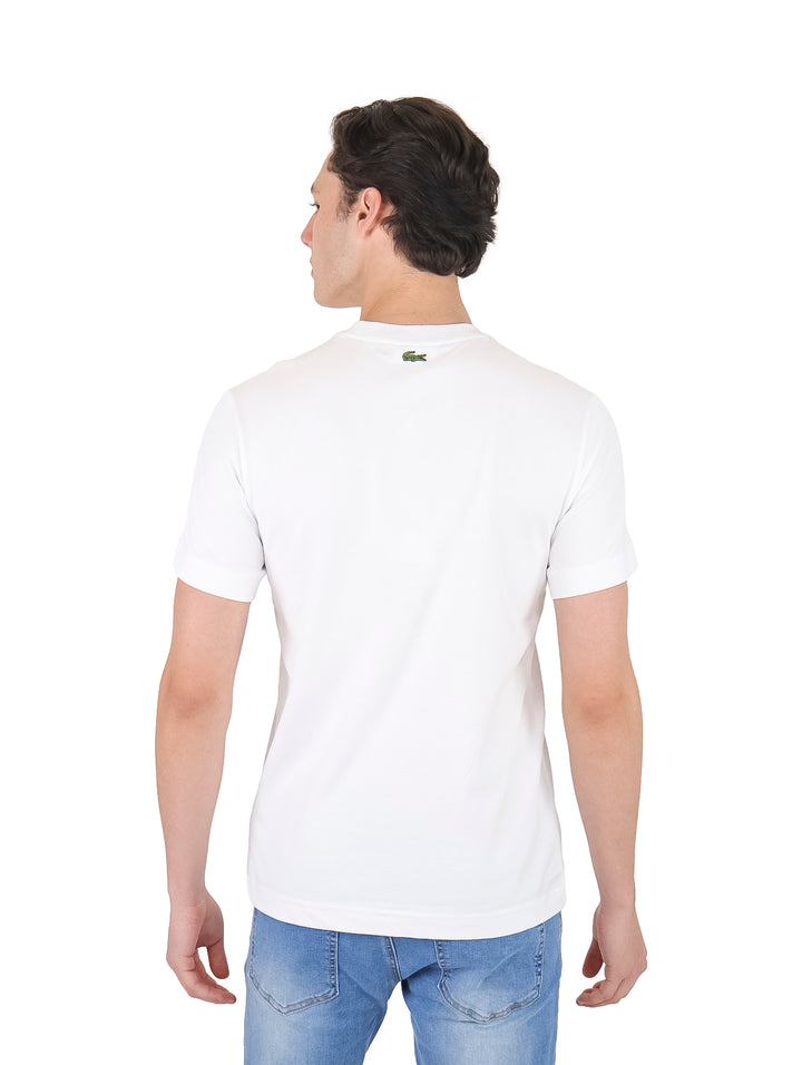 Hombre vistiendo camiseta blanca de manga corta con cuello redondo y pequeños logos verdes en el pecho.