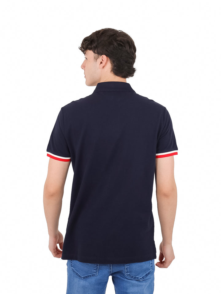 Hombre vistiendo polo azul marino con franjas horizontales blanca y roja en el pecho.