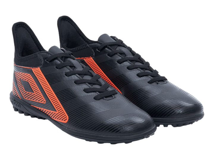 Zapato de fútbol Umbro negro con diseño geométrico naranja y suela para césped sintético.