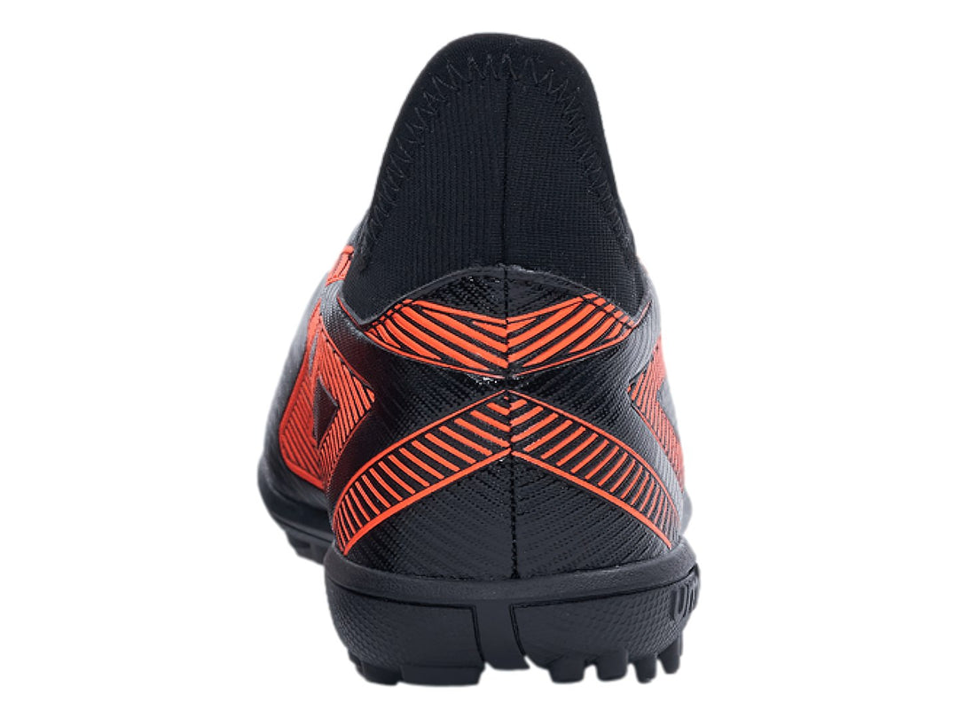 Zapato de fútbol Umbro negro con diseño geométrico naranja y suela para césped sintético.