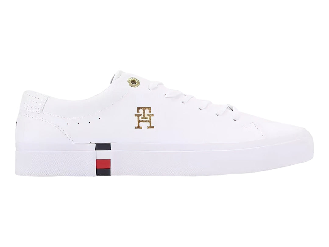 Tenis blancos Tommy Hilfiger de perfil bajo con detalles en dorado y franja roja, blanca y azul en la suela.