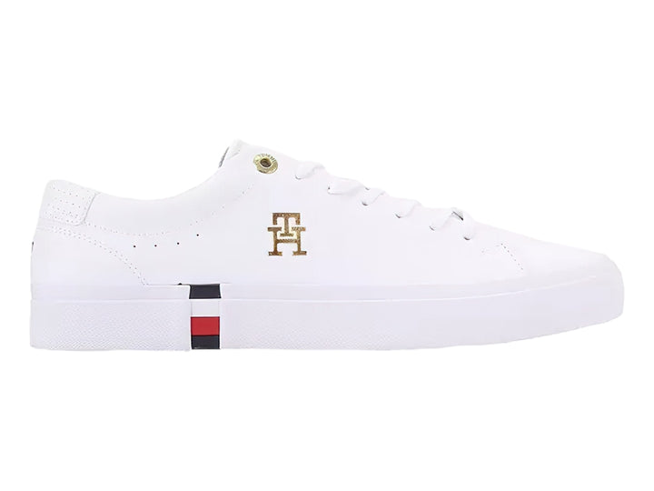 Tenis blancos Tommy Hilfiger de perfil bajo con detalles en dorado y franja roja, blanca y azul en la suela.