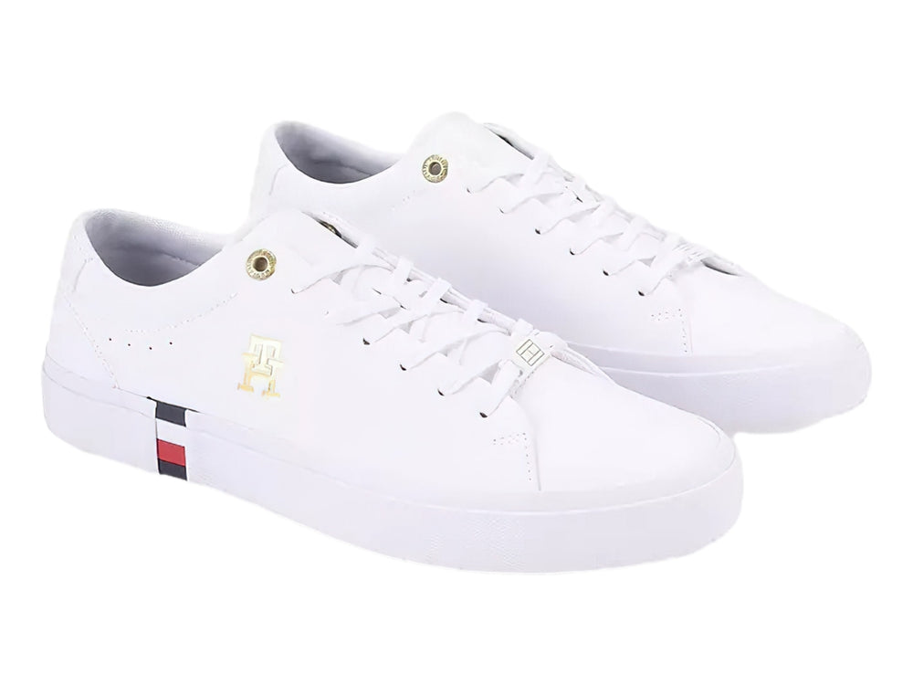 Tenis blancos Tommy Hilfiger de perfil bajo con detalles en dorado y franja roja, blanca y azul en la suela.