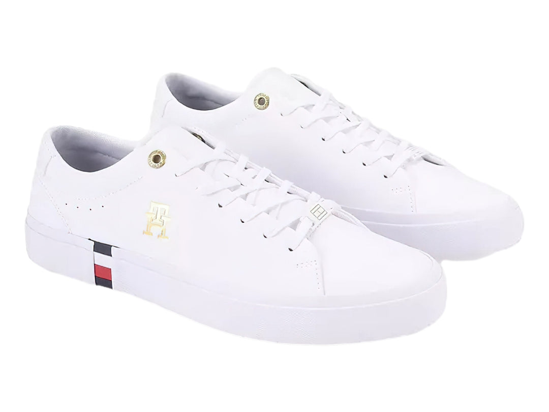 Tenis blancos Tommy Hilfiger de perfil bajo con detalles en dorado y franja roja, blanca y azul en la suela.