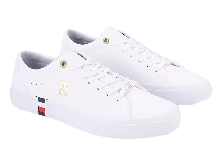 Tenis blancos Tommy Hilfiger de perfil bajo con detalles en dorado y franja roja, blanca y azul en la suela.