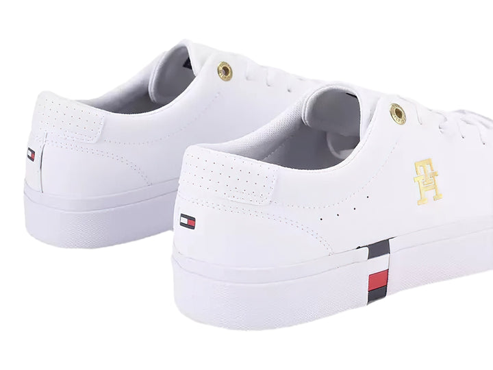 Tenis blancos Tommy Hilfiger de perfil bajo con detalles en dorado y franja roja, blanca y azul en la suela.