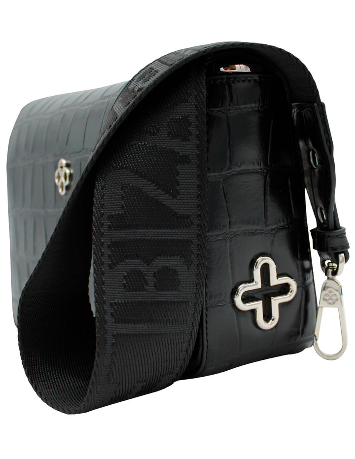 Bolso de hombro negro con textura de cocodrilo, correa ancha tejida y detalle metálico en forma de cruz.