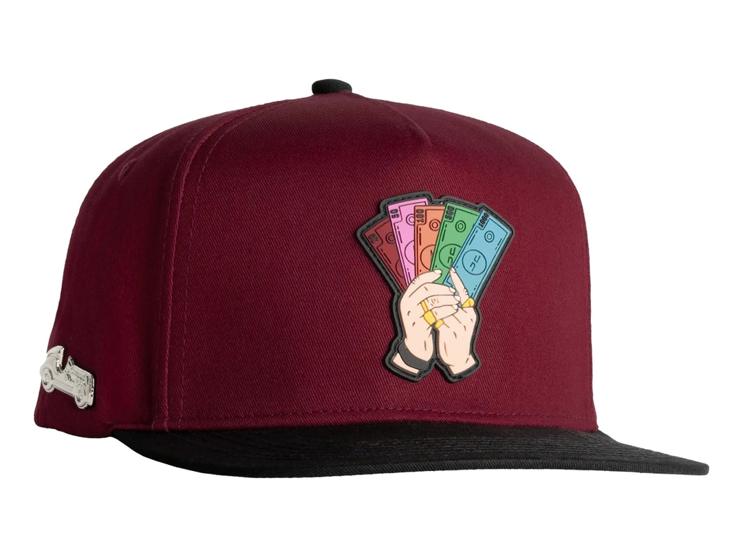 Gorra snapback color rojo con visera negra y un parche bordado frontal de manos sosteniendo billetes.