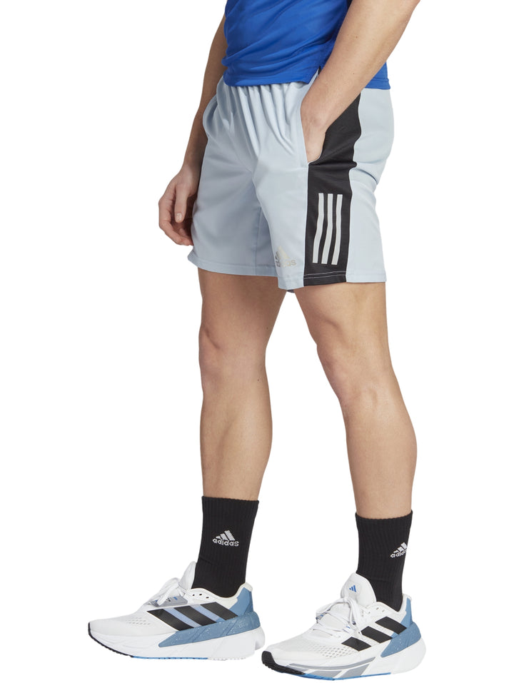 Hombre vistiendo shorts deportivos Adidas color azul claro con franjas negras laterales.
