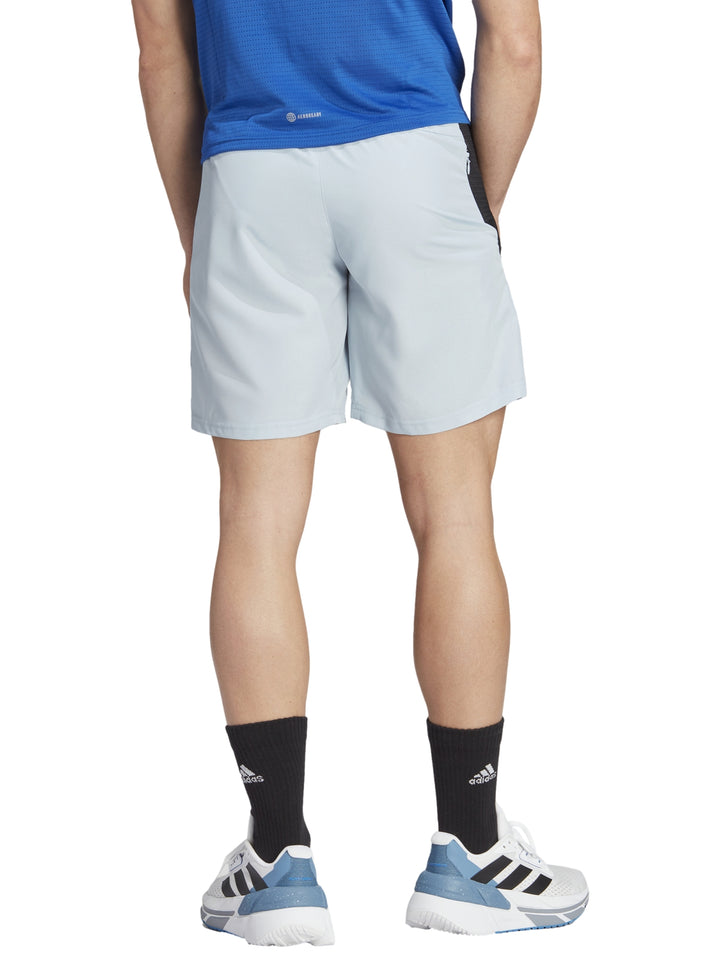 Hombre vistiendo shorts deportivos Adidas color azul claro con franjas negras laterales.