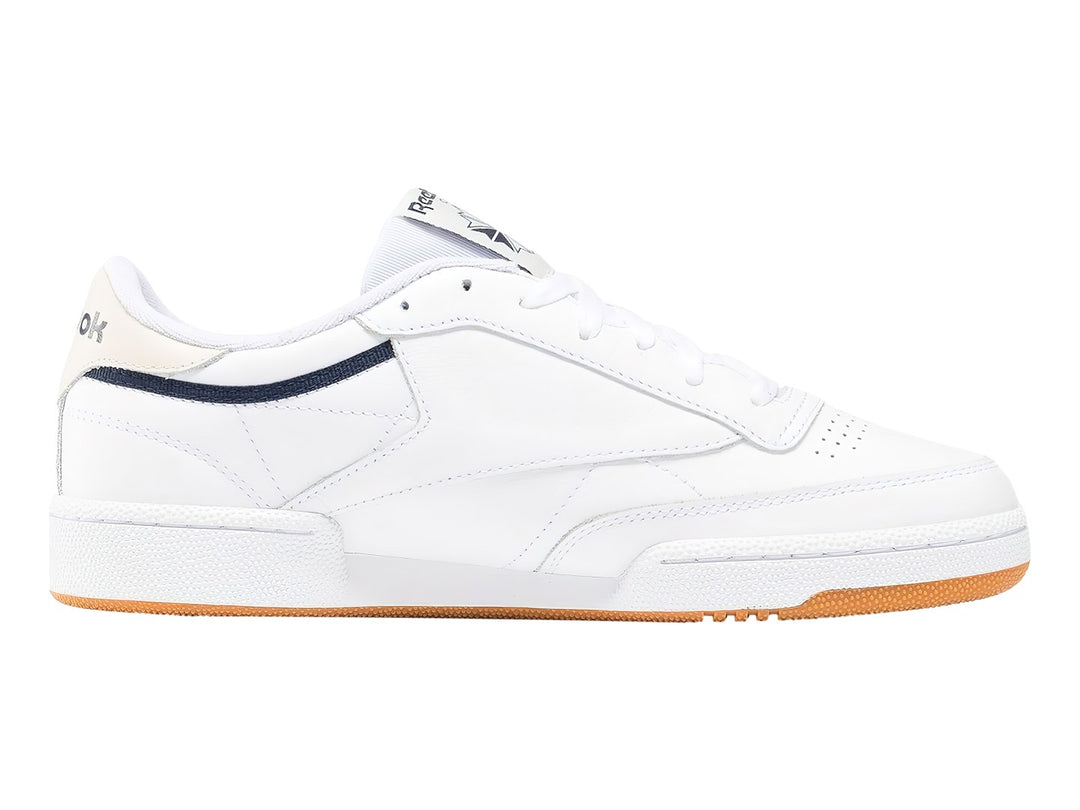Tenis Reebok Club C 85 blancos con suela de goma color miel y detalle lateral en azul marino.