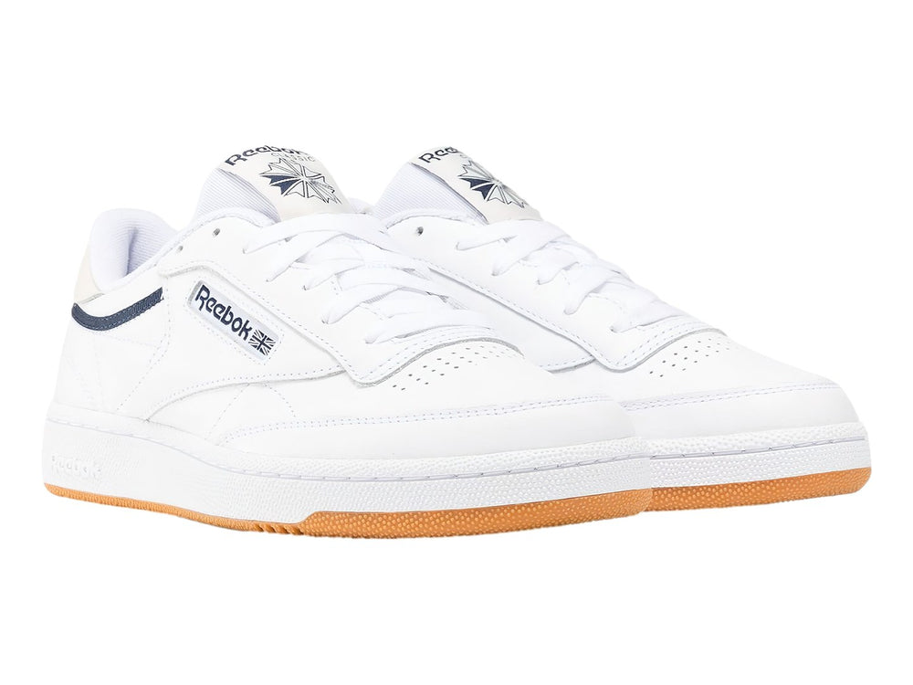 Tenis Reebok Club C 85 blancos con suela de goma color miel y detalle lateral en azul marino.