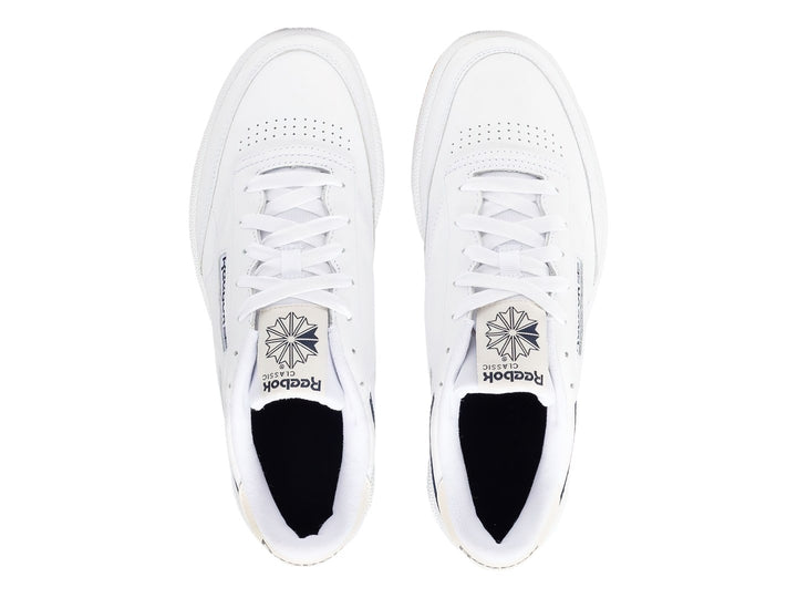 Tenis Reebok Club C 85 blancos con suela de goma color miel y detalle lateral en azul marino.