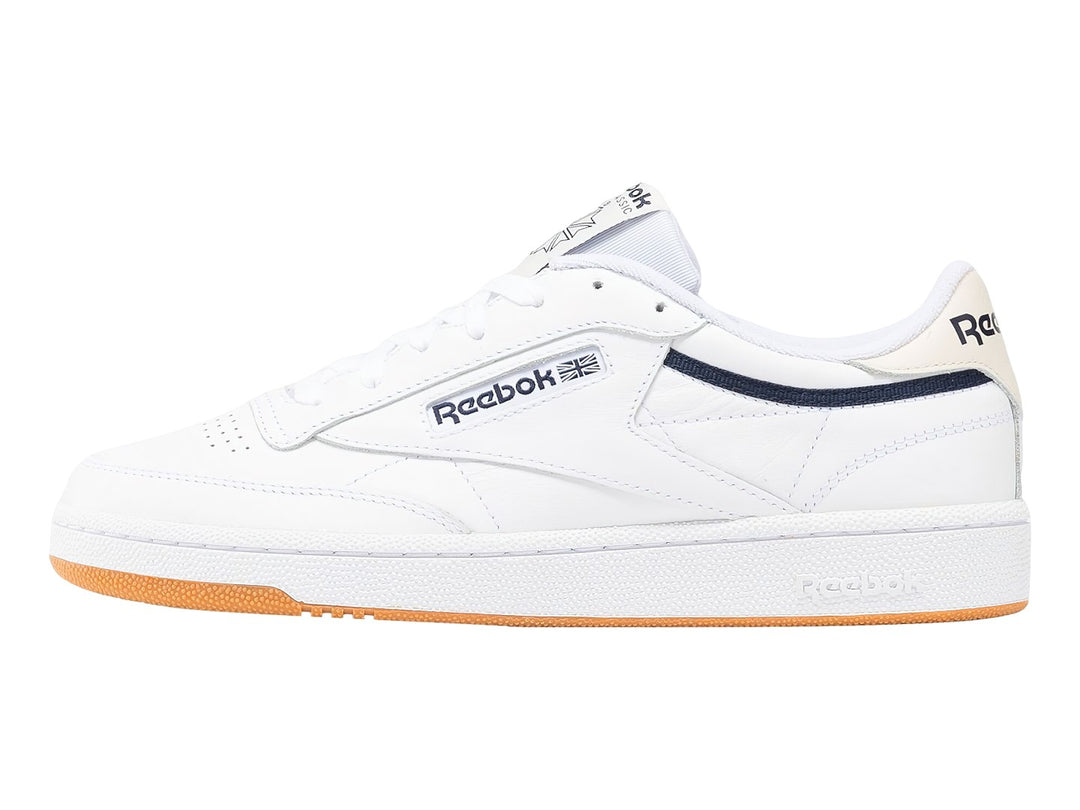 Tenis Reebok Club C 85 blancos con suela de goma color miel y detalle lateral en azul marino.