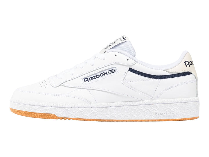 Tenis Reebok Club C 85 blancos con suela de goma color miel y detalle lateral en azul marino.
