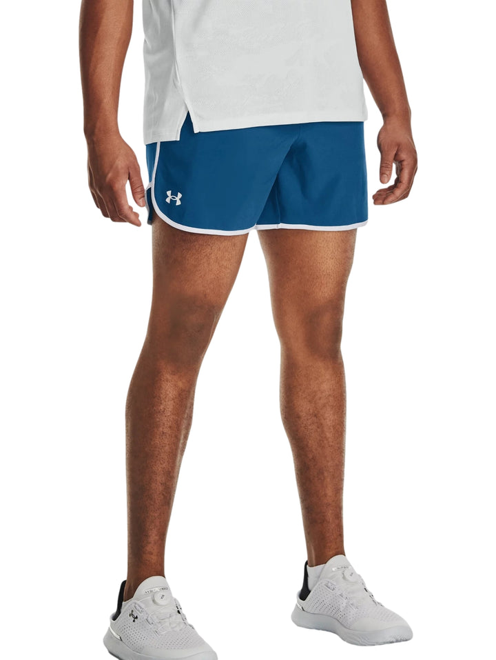 Hombre vistiendo shorts deportivos color azul con ribete blanco de la marca Under Armour.