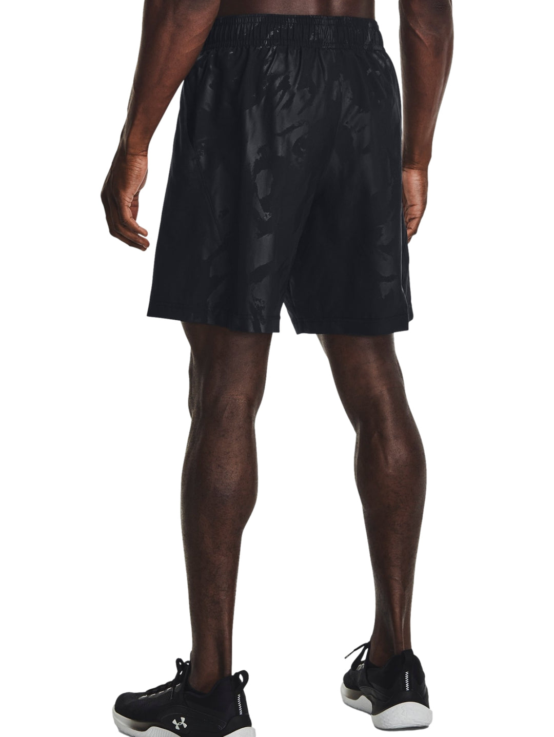 Hombre vistiendo shorts deportivos negros con un patrón grabado sutil de la marca Under Armour.