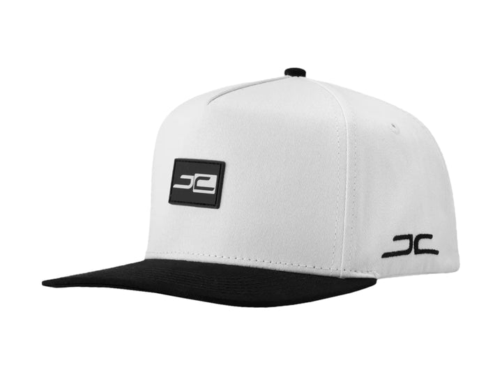 Gorra snapback blanca con visera plana negra y logotipos JC en contraste.