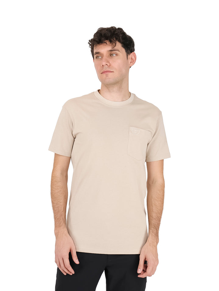 Hombre vistiendo una playera color beige de manga corta con un bolsillo pequeño en el pecho.