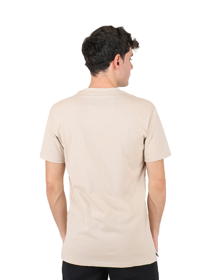 Hombre vistiendo una playera color beige de manga corta con un bolsillo pequeño en el pecho.