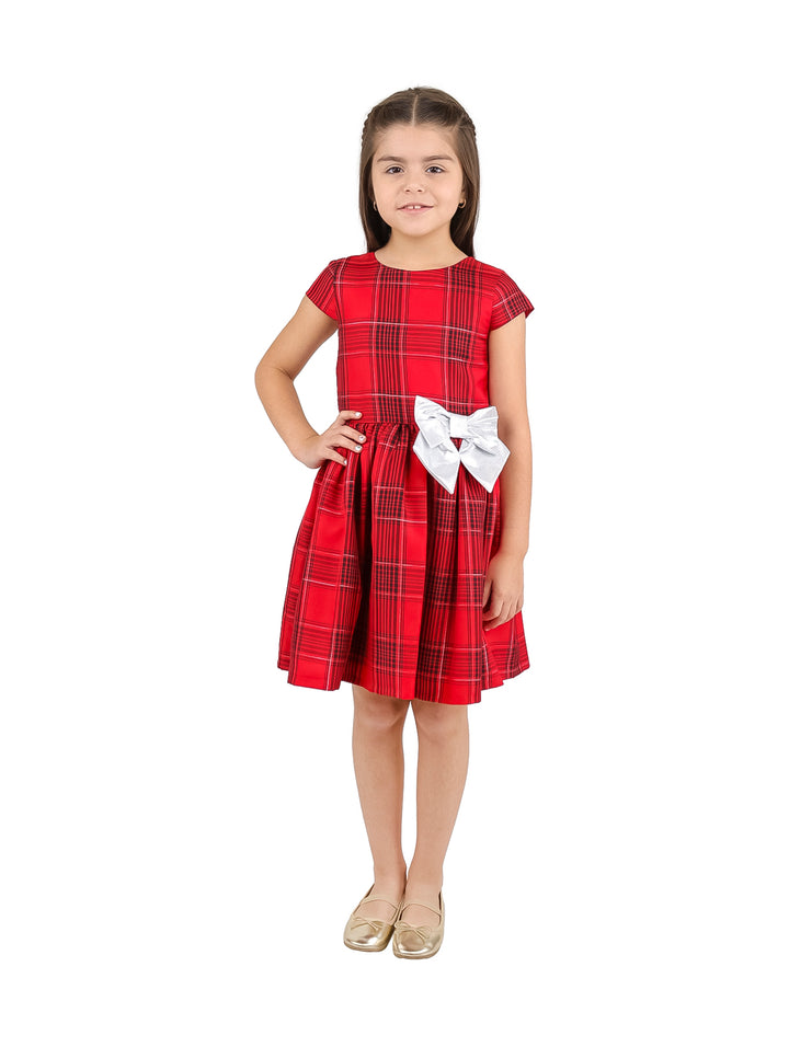 Niña vistiendo un vestido rojo a cuadros con un moño blanco en la cintura.