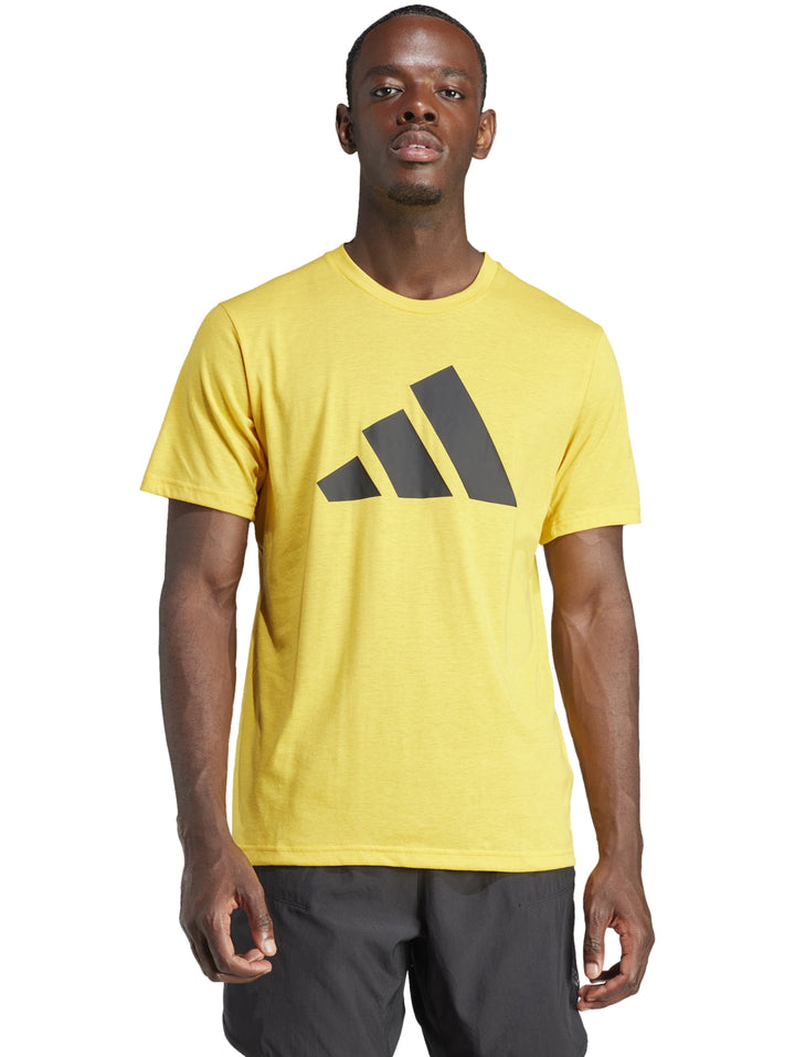 Hombre vistiendo una playera Adidas de color dorado con un logotipo grande en negro en el pecho.