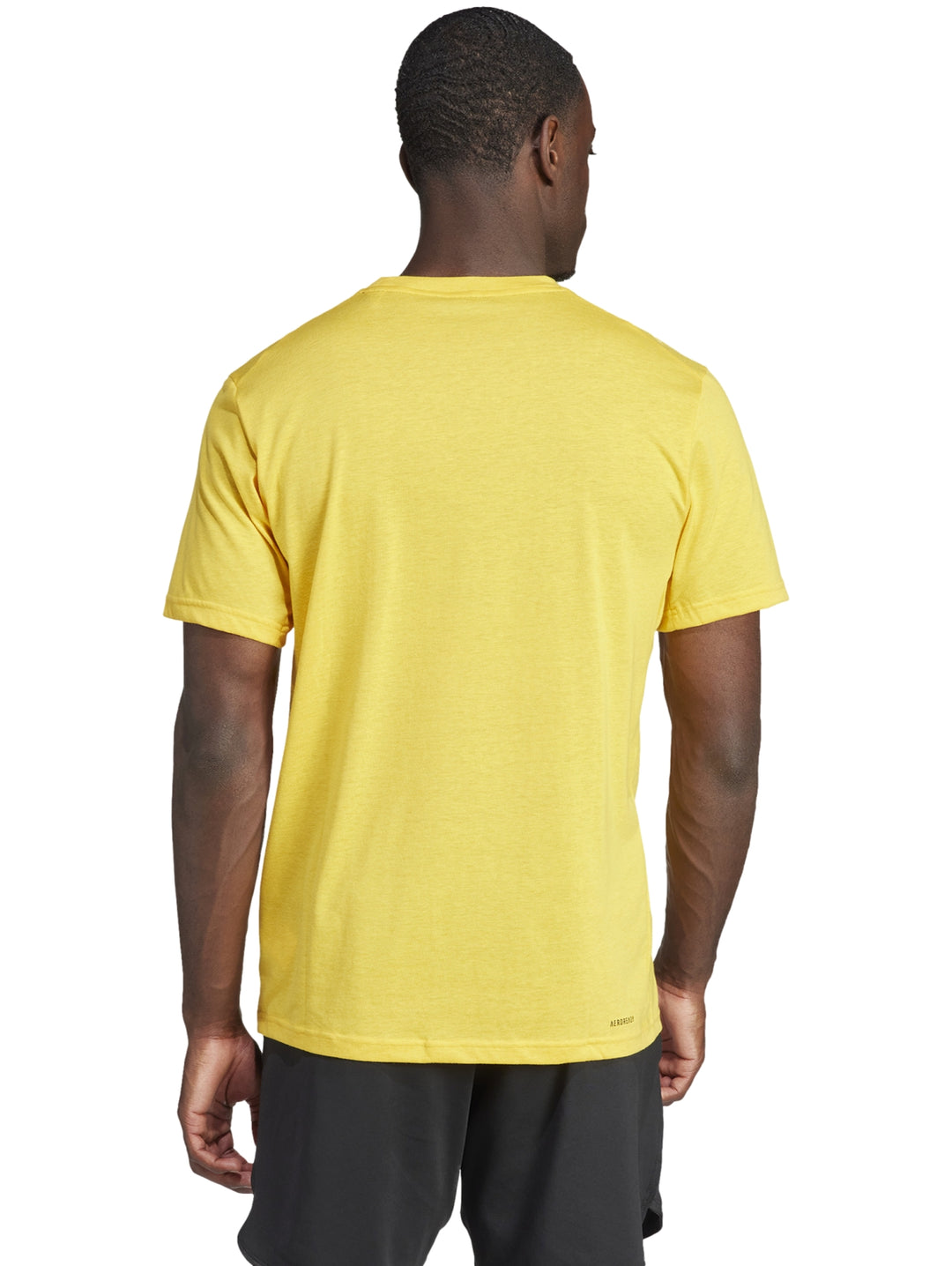 Hombre vistiendo una playera Adidas de color dorado con un logotipo grande en negro en el pecho.