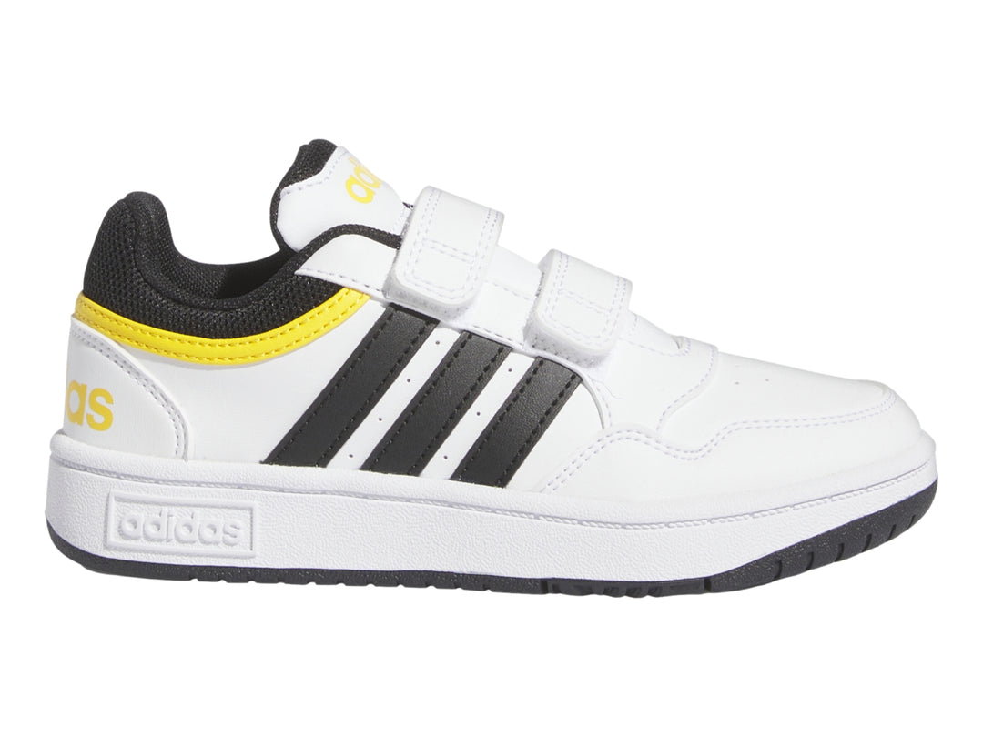 Tenis Adidas blancos con tres franjas negras, detalles amarillos y cierre de velcro.