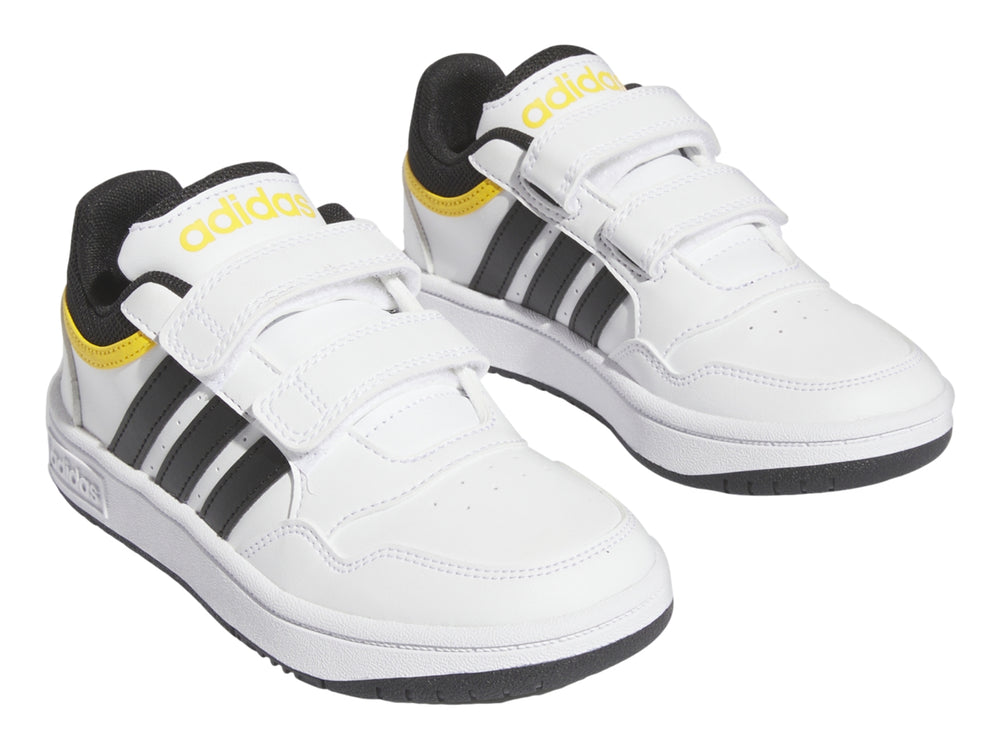 Tenis Adidas blancos con tres franjas negras, detalles amarillos y cierre de velcro.