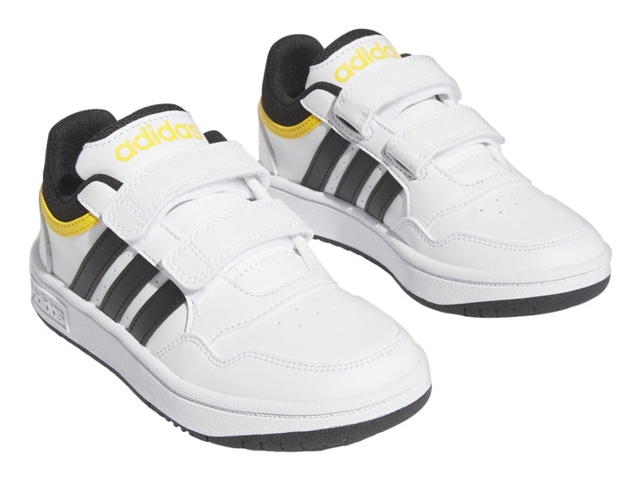 Tenis Adidas blancos con tres franjas negras, detalles amarillos y cierre de velcro.