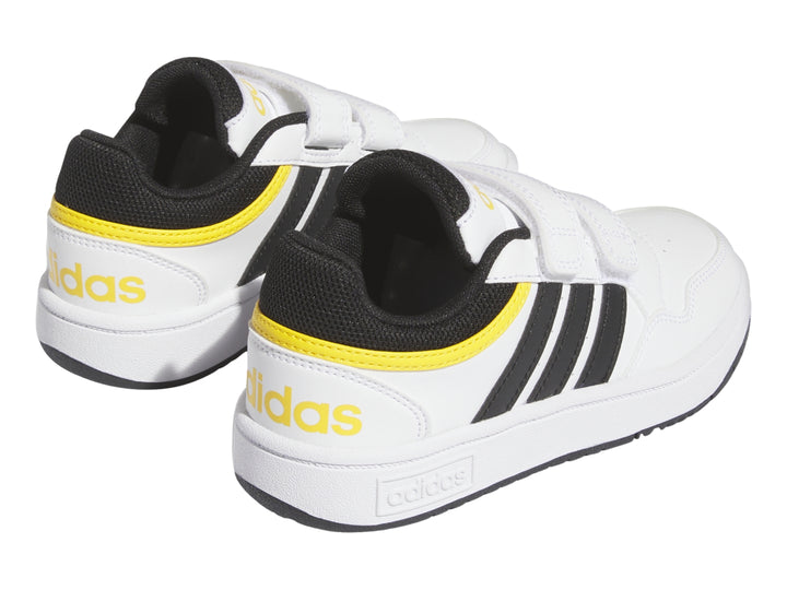 Tenis Adidas blancos con tres franjas negras, detalles amarillos y cierre de velcro.