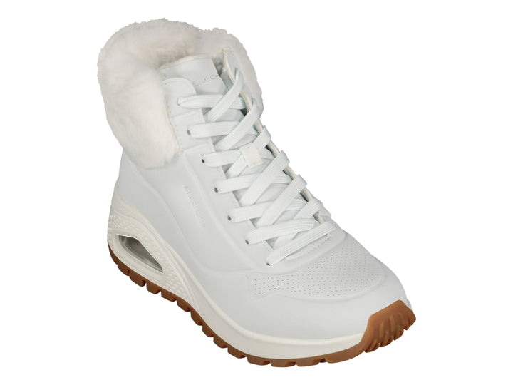Botín deportivo Skechers blanco con forro interior de peluche blanco y suela color café.